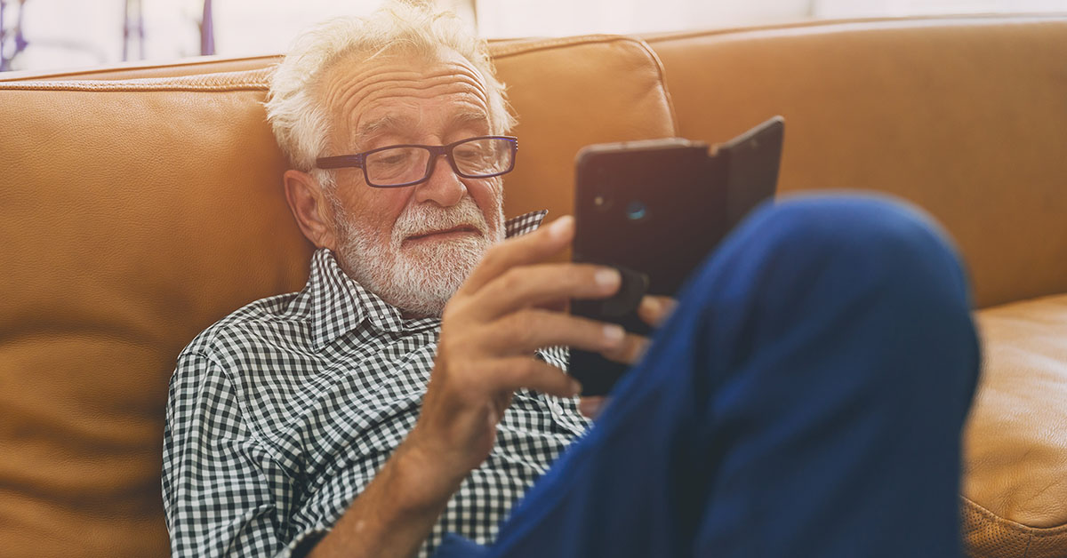 Eldre mann i sofa som ser på mobiltelefonen